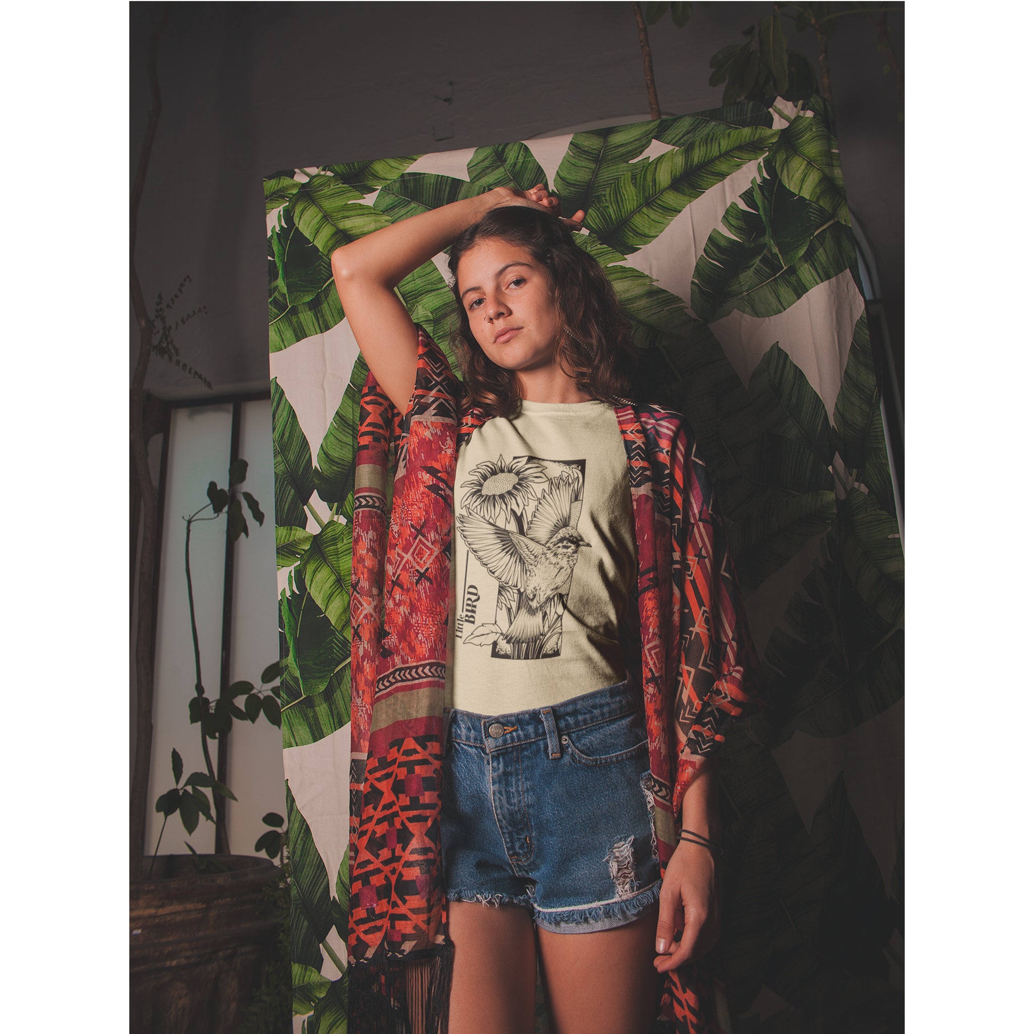 Person wearing a graphic t-shirt and colorful jacket in front of a leafy background – Bamerix